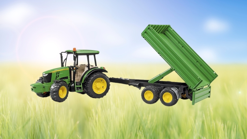 John Deere farm tractor toy with a functional green trailer displayed in a grassy field under a bright sky